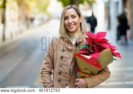 Positive Female Standing With Hand In Pocket Of Warm Coat With Bouquet Of Red Poinsettia Flowers And