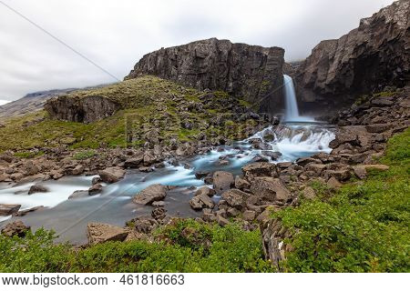 Waterfall In A Rocky Country With Green Bushes Around In Iceland