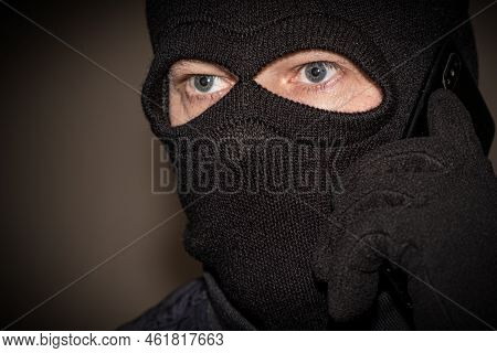 Young Adult In Black Clothes With Hidden Face. Ill-intended Fraudster Uses Mobile. Fraudster Calls. 