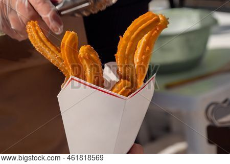 Chef Woman Holding Paper Box With Homemade Crunchy Churros At Summer Outdoor Food Market - Close Up.