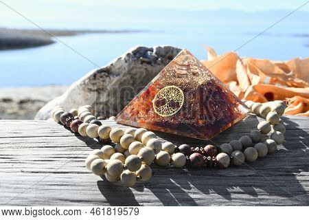 An Image Of And Orgonite Pyramid And Prayer Necklace On A Piece Of Weathered Driftwood.
