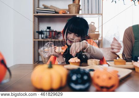 Young Girl And Mother At Halloween Making Treats And Cupcake On Table. Happy Halloween Day