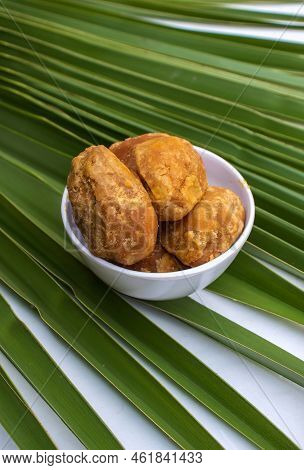 Closeup Of Organic Palm Jaggery Or Gur In A White Bowl Isolated On A Palm Leaf In Vertical Orientati