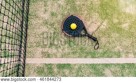 Top View Of Yellow Ball Over Padel Tennis Racket Behind Net In Green Court