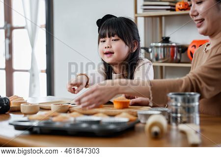 Young Girl And Mother At Halloween Making Treats And Cupcake On Table. Happy Halloween Day