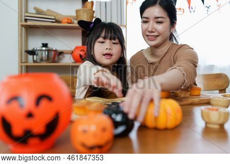 Young Girl And Mother At Halloween Making Treats And Cupcake On Table. Happy Halloween Day