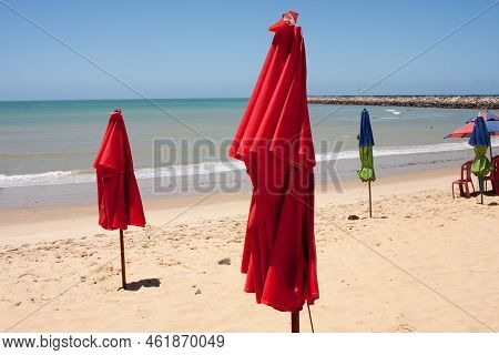 Red Folded Umbrellas Stuck In The Sandy Shoreline At Iracema Beach In Fortaleza, Brazil