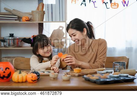 Young Girl And Mother At Halloween Making Treats And Cupcake On Table. Happy Halloween Day