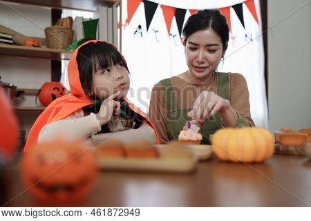 Young Girl And Mother At Halloween Making Treats And Cupcake On Table. Happy Halloween Day