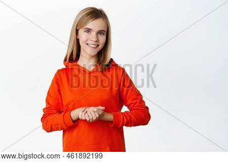 Portrait Of Cute Smiling Schoolgirl, Beautiful Blond Girl Standing In Polite Pose, Holding Hadns Tog