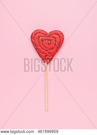Red And White Candy On A Stick In The Shape Of A Heart On A Pink Background. Minimal Concept Of Swee