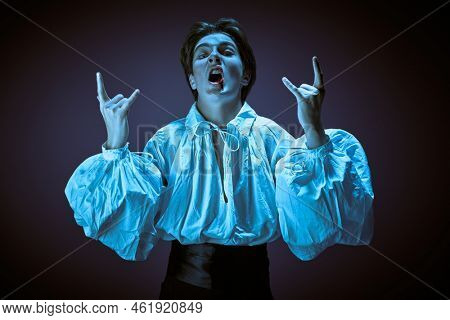 Expressive teenage vampire in elegant white shirt sings and dances with verve on a rock party. Halloween vampire party. Studio portrait. 