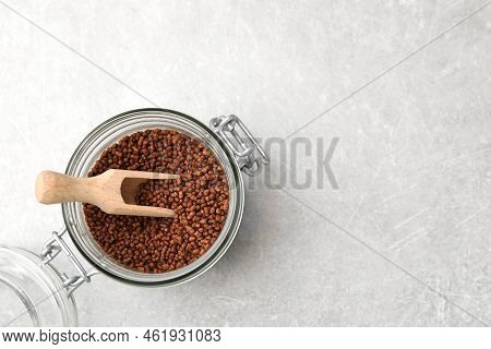 Glass Jar With Wooden Scoop And Buckwheat Tea Granules On Light Grey Table, Top View. Space For Text