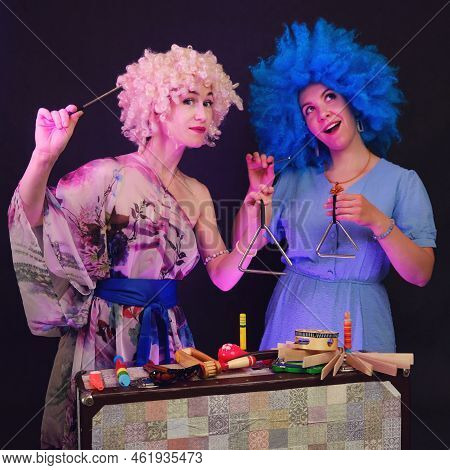 Happy Women In Funny Wigs Give A Musical Performance On A Studio Black Background. Smiling Women Sho