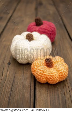 Three Pumpkins Crocheted Stand On A Wooden Table. Autumn Decorations For Halloween. On A Wooden Tabl