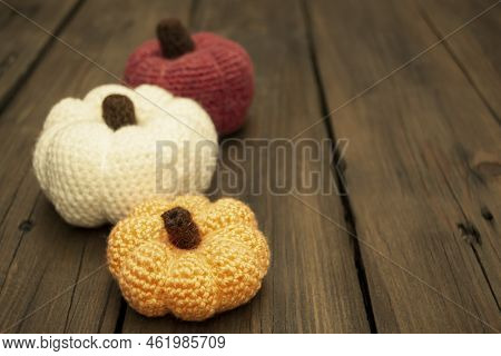 Three Pumpkins Crocheted Stand On A Wooden Table. On A Wooden Table, Knitted Pumpkins Stand In A Row