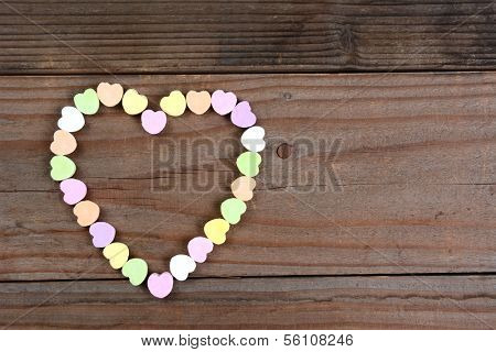 Overhead view of a group of Valentines Day candy on a rustic wood table arranged in a heart shape. Horizontal format with copy space.