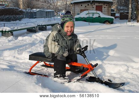 Little Boy Sitting On A Sled On The Street