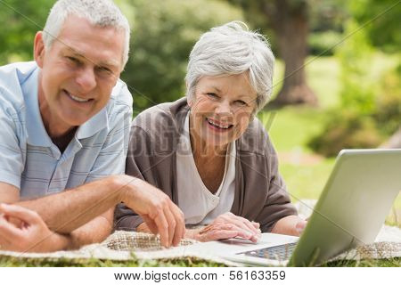 Smiling senior couple using laptop while lying at the park