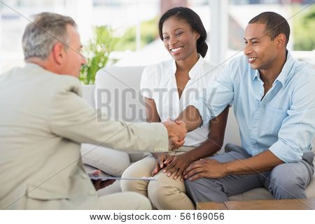 Young couple shaking hands with salesman on the couch in the office
