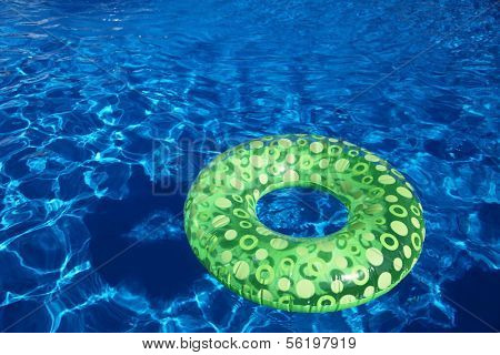 An inflatable green plastic ring swimming in a shiny blue swimming pool.