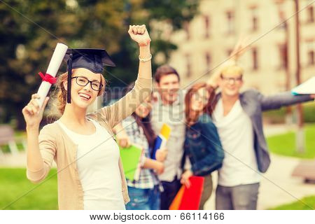 education, campus and teenage concept - smiling teenage girl in corner-cap and eyeglasses with diploma and classmates on the back