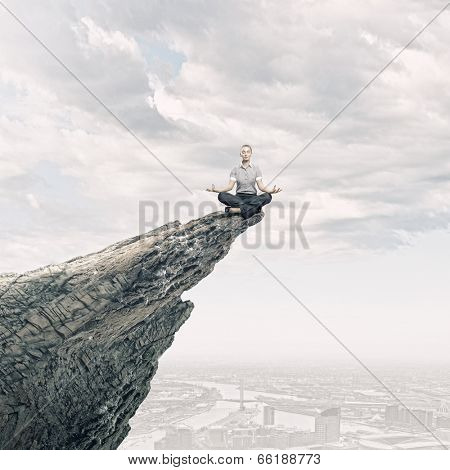 Young businesswoman sitting lotus pose on edge of rock mountain