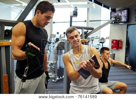sport, fitness, lifestyle and people concept - men with clipboard taking notes and exercising on gym machine
