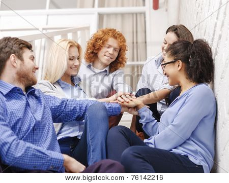 business, office, gesture and startup concept - smiling creative team with hands on top of each other sitting on staircase