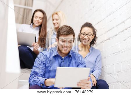 business, technology and startup concept - smiling creative team with tablet pc computer sitting on staircase