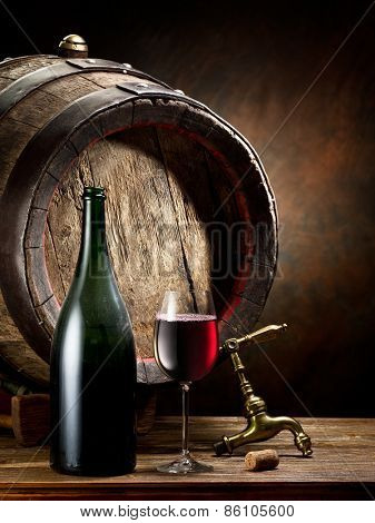 Still-life with glass of wine, bottle and barrel on the table in the cellar.