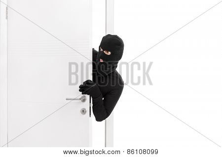 Studio shot of a stealthy thief breaking into a room through a door and carefully looking around isolated on white background