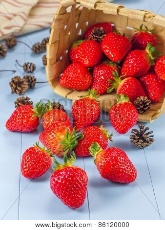 Basket With Strawberries And Fir Cones Spilling On A Table