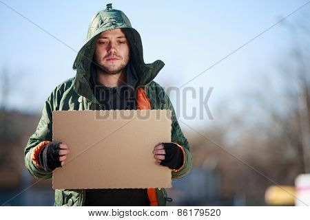 Homeless person with blanck cardboard. Focused on cardboard