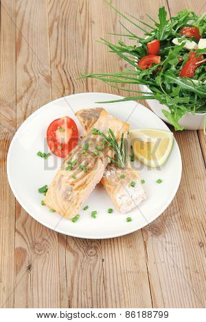 savory fish portion : roasted norwegian salmon chunks and vegetable salad on white dish over wooden table