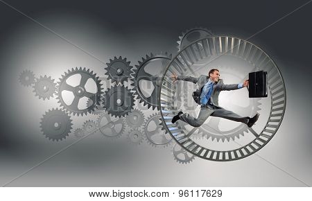 Young businessman running in wheel of gears mechanism