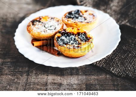 Egg tart - creamy sweet curstard on white plate on wooden table close up with copy space. Pasteis de Belem dessert
