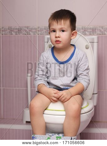 Little boy sitting in the bathroom on the toilet room