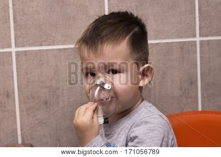 Cute boy inhalation therapy by the mask of inhaler. Close up image of a little kid with respiratory problem or asthma. Sick boy with clear oxygen mask.