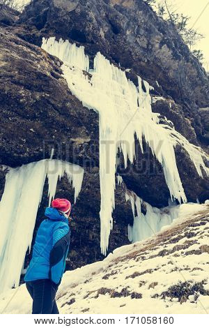 Active young woman looking at frozen icicles. Exploring Pericnik waterfall in Vrata valley, Slovenia.