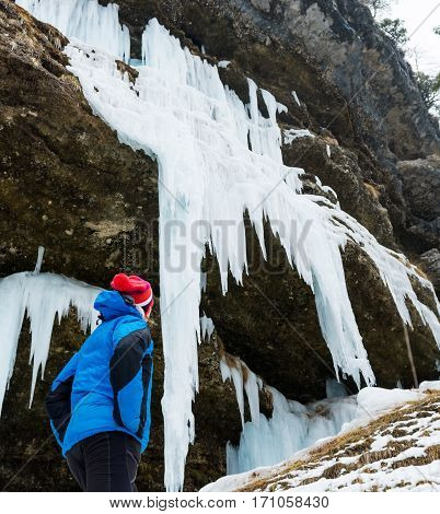 Active young woman looking at frozen icicles. Exploring Pericnik waterfall in Vrata valley, Slovenia.