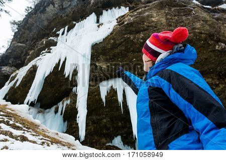Active young woman looking at frozen icicles. Exploring Pericnik waterfall in Vrata valley, Slovenia.