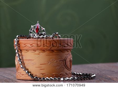 metal beads and a ring with a red stone on small closed birch bark casket on green fabric background
