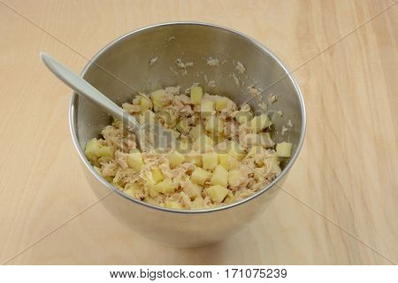 Mixing together apple cubes and albacore tuna fish in stainless steel mixing bowl with plastic spoon