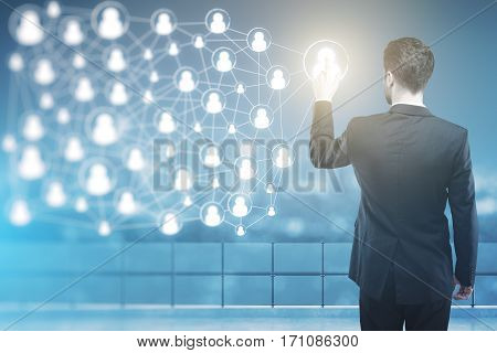 Back view of businessman in suit pointing at abstract connected people icons at night. HR and network concept