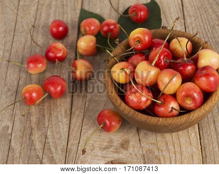 Background of ripe cherries. Pile of fresh and tasty cherries in wooden bowl. Fresh cherries scattered on a wooden table.