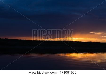 Evening on the river. Dark sky and the falling sun