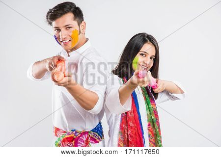 young indian couple holding pichkari on Holi festival, standing isolated over white background with copy space
