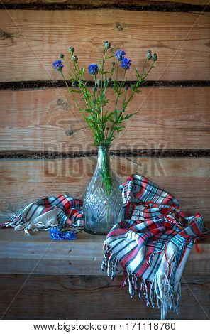 Beautiful still life with blue flowers in a glass vase and a beautiful shawl in the old rural wooden house