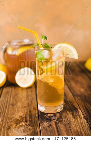 Lemon ice tea on brown wooden table with lemons around. Iced tea with lemon slices and mint on rustic background